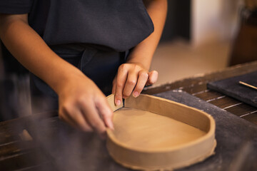 Hands of girl works with clay in modern pottery workshop. The pr - obrazy, fototapety, plakaty
