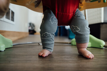 Low view of baby's chubby legs while standing in jumper at home.