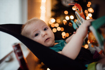 Close up of baby in bouncer looking towards camera with Christma