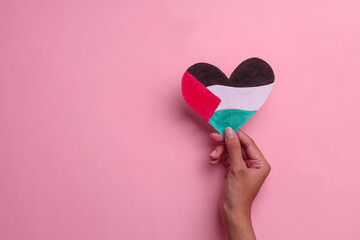 Hand holding the heart shape paper symbolize Palestine flag over pink background - obrazy, fototapety, plakaty