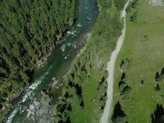 Aerial view of a green mountain landscape and alpine meadows where a river flows from the mountains and a beautiful coniferous forest stretches.