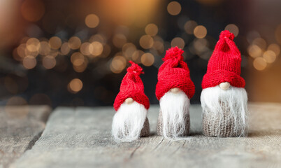 three Christmas gnomes on a wooden table against a background of defocus lights