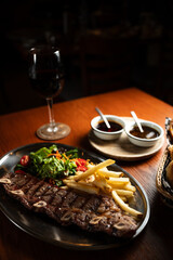 Strip roast with french fries and salad on wooden table with glass of red wine. Argentine restaurant concept. Gastronomy concept