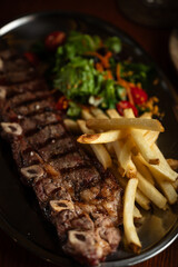 Strip roast with french fries and salad on wooden table with glass of red wine. Argentine...