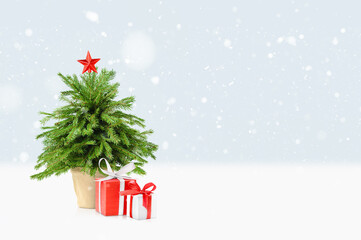 small Christmas tree and two gifts under it on a winter background