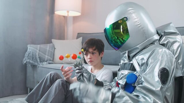 Father and son play in the living room at home, man in an astronaut costume sitting on the floor with her son, boy playing with a toy model of the solar system, study of astronomy.