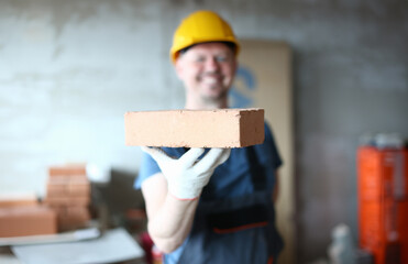Focus on male hand presenting concrete block. Happy smiling constructor man in protective outfit...