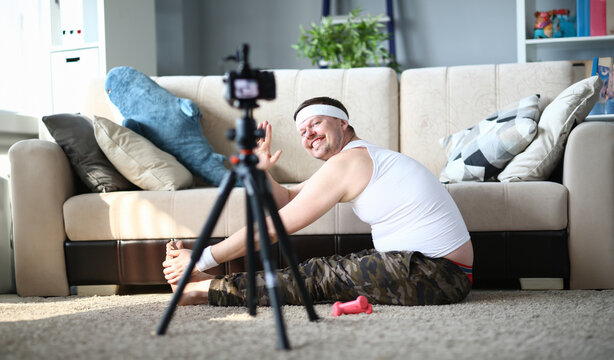 Happy Man Recording Stretching Exercise on Camera. Smiling Blogger Guy Shooting Video on Digital Camera for Sport Blog. Bearded Male Practice Fitness for Muscles Sitting on Floor in Apartment