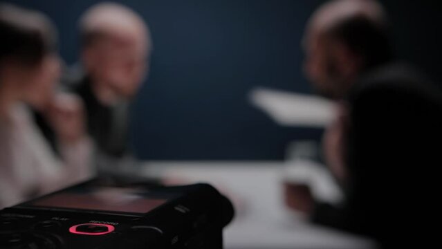 Digital voice audio dictophone, close up blinking rec button. Interrogation by police officers detectives. FBI agent shows evidence. Suspect denies accusations of his guilt. Arrested mafia