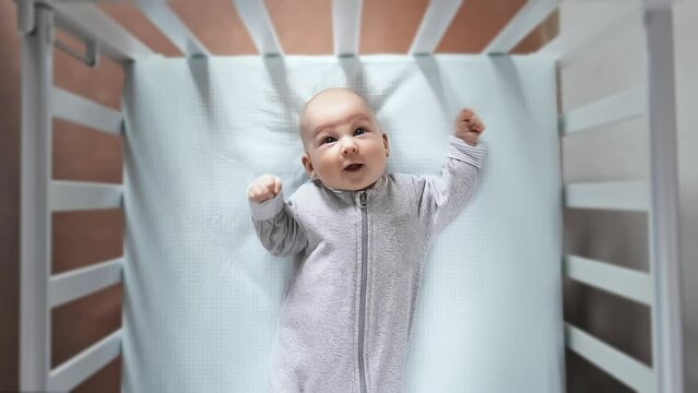 Little one infant is lying in the crib looking up. 2 or 3 month old baby is lying in the bed and doesn't want to sleep. Without a parent