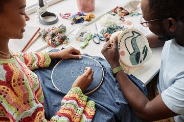 Close-up of two African American designers making stylish embroidery with threads and beads on...