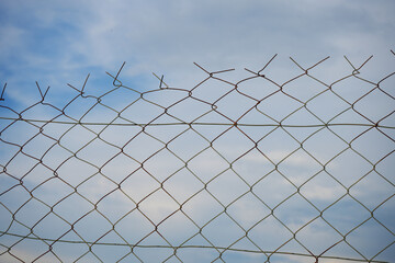 Looking up at a chain link fence with blue sky and clouds. wire fence. Chain link fence see sky. Opening in metallic fence. blue sky. Challenge. breakthrough concept.