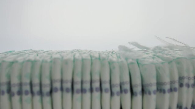 Stack of baby diapers with light feathers on a white background. Concept of lightness, softness and comfort when wearing diapers. Cotton. Copy space for text, slow motion