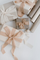 Holiday gift boxes packaging process. Beautiful beige colour gifts with ribbon bows on white background. Flat lay, top view