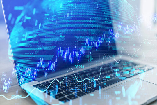 Close up of laptop on desk with glowing candlestick forex chart on blurry background. Stock market, trading analysis and investment concept. Toned image. Double exposure.