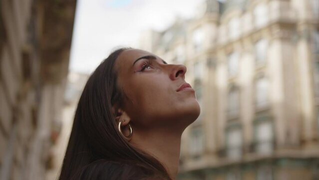 Close up, orbiting view, beautiful brunette woman looking up at Paris buildings