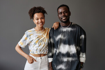 Happy young African American couple in trendy tie dye attire looking at camera during photo shooting while standing next to one another