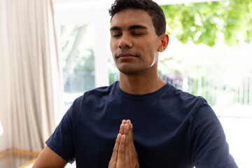 Biracial man doing yoga and meditating at home