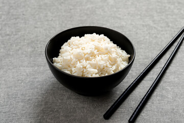 cereal breakfasts. white boiled rice lies in a black deep plate with black Chinese chopsticks on a gray table