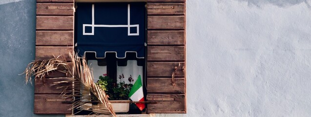 Bello particolare di facciata con serramento e tenda colorata con vaso di fiori e bandiera italiana