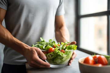 Obraz na płótnie Canvas Man eat healthy lunch in modern interior, Unrecognizable profile male torso in green t-shirt, hand with fork, near window with vegetable salad in bowl, diet food concept