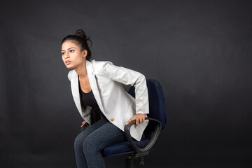 Cheerful young female model in casual wear wearing white jacket, black top and black jeans posing with a chair. Shoot for advertisement.