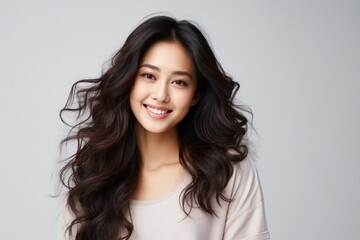 Naklejka premium Portrait of a smiling young Asian woman with flowing hair on a light background.