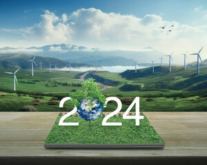 2024 white text with planet and tree on green grass on open book on table over wind turbine farm on mountain, Happy new year 2024 ecological cover, Elements of this image furnished by NASA - obrazy, fototapety, plakaty