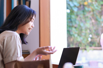 excited asian woman sitting in cafe using laptop to online meeting raise palm do presenting gesture...