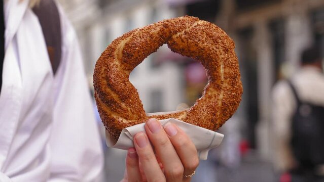 Girl tourist holding simit close-up on city street on sunny day without face. Turkish bagels with sesame seeds. Popular Turkish street food simit. Simit background, side view