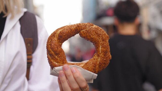 Tourist girl holding Simit close-up on Istiklai city street with red retro driveway, on sunny day without face. Turkish bagels with sesame seeds. Popular Turkish Street Food Simit.