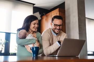 Young father works on laptop while his wife looks after child.Work from home parenting telecommuting