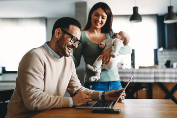Portrait of business man using laptop working while family in background at home.