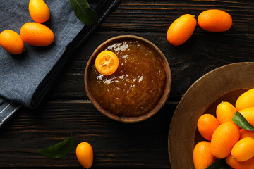 Kumquat on plate, jam in bowl and towel on dark wooden background, top view