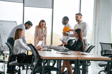 Against the panoramic window, having a meeting. Group of office workers are together indoors