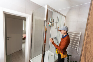 young foreman measuring shower cabin in modern bathroom.