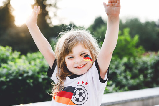 Little blond preschool girl watching soccer football cup game on public viewing. Happy joyful excited child about winning game match of favorite national football team. girl with German flag on face.