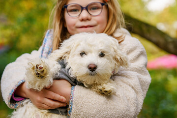 Little girl playing with her pet dog Maltese in park. Happy child and cute puppy.