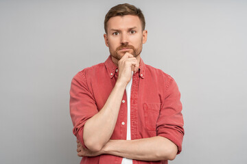 Serious man holds chin. Middle aged man putting palm fingers to face, looking at camera with pensive look, thinking, pondering, not smiling, dissatisfied disappointed emotion isolated gray background