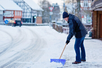 Man with snow shovel cleans sidewalks in winter during snowfall. Winter time in Europe. Young man...
