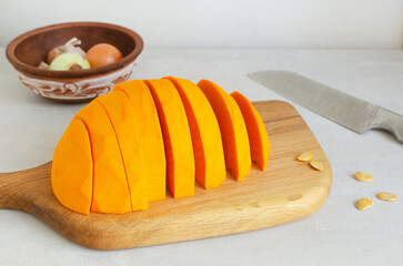 Half of a Hokkaido pumpkin, pitted and cut into pieces, lies on a cutting board. The process of cooking autumn cream soup. Concept of healthy food. Vegan and vegetarian dishes. Horizontal orientation.