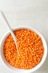 Orange lentils in a white bowl with a teaspoon on a light background. The concept of proper...