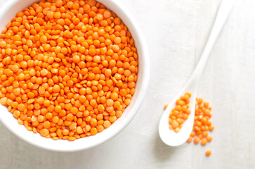 Orange lentils in a white bowl with a teaspoon on a light background. The concept of proper nutrition. Vegan and vegetarian food. Horizontal orientation. Top view.