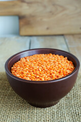 Orange lentils in a brown ceramic bowl on a cutting board on a wooden table. The concept of proper nutrition. Vegan and vegetarian food. Rustic style. Vertical orientation.
