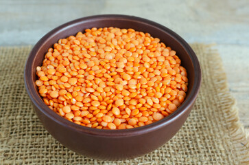 Orange lentils in a brown ceramic bowl on a cutting board on a wooden table. The concept of proper nutrition. Vegan and vegetarian food. Rustic style. Horizontal orientation.