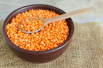 Orange lentils in a brown ceramic bowl with teaspoon on a cutting board on a wooden table. The...