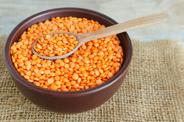 Orange lentils in a brown ceramic bowl with teaspoon on a cutting board on a wooden table. The concept of proper nutrition. Vegan and vegetarian food. Rustic style. Horizontal orientation.