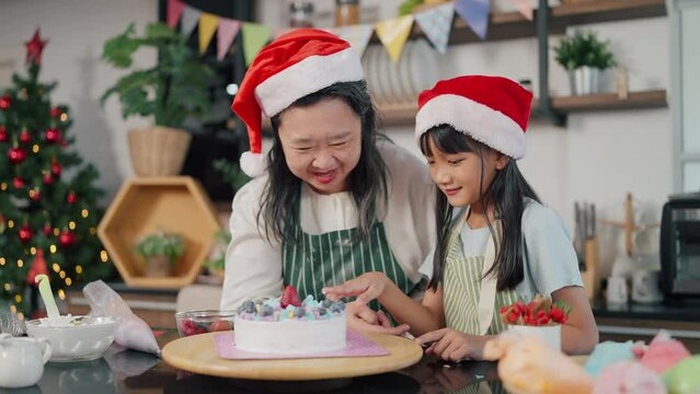 Happy Grandmother and granddaughter playful while making cake for Christmas day in kitchen room at home. Christmas cake decorated. Festive holiday. Family and cooking concept