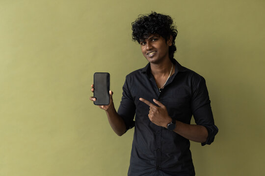 Young indian boy holding a mobile phone and point towards it's screen. Mobile phone with a green screen for mockup.
