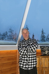thoughtful mature charismatic man, senior 60 years old in plaid shirt sits by window, emotional...